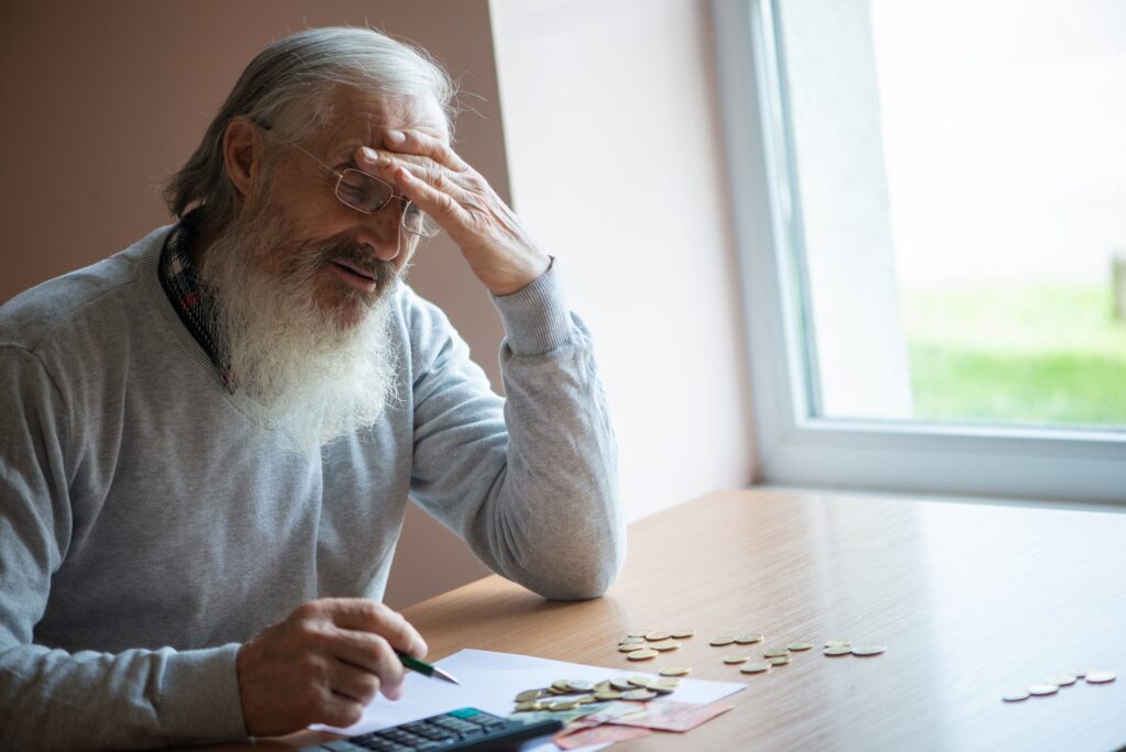 Old bearded senior man with calculator and bills counting euro money and writing notes
